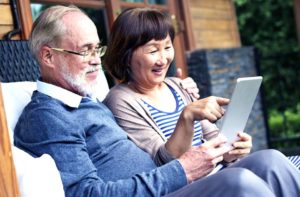 older asian husband and wife sitting together viewing a tablet